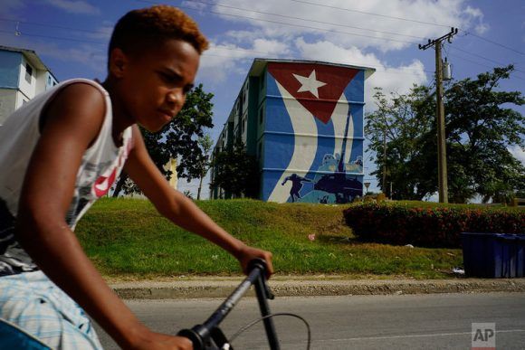 Un niño pasea en bicicleta frente a un mural con la bandera cubana y una imagen de Fidel Castro saltando de su tanque durante la invasión de Playa Girón. Guantánamo, Cuba, 25 de julio del 2018. Foto: Ramón Espinoza